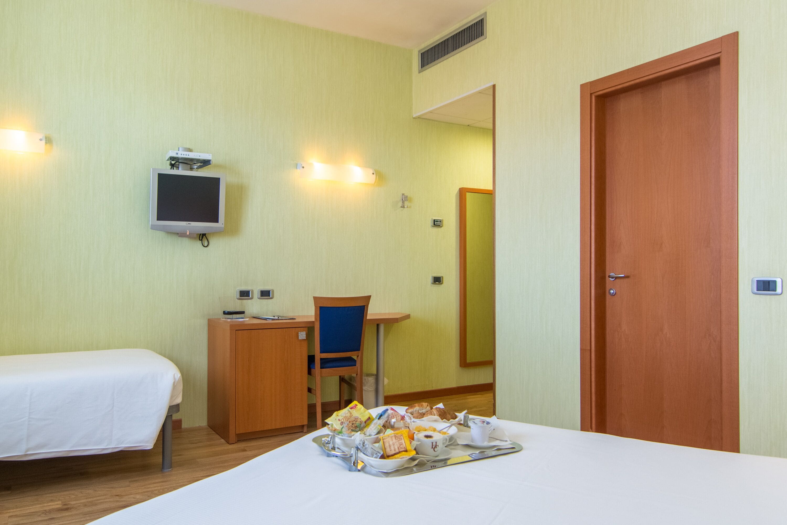 Une chambre d’hôtel comprenant un lit, un bureau avec une chaise, une télévision et un plateau avec des articles pour le petit-déjeuner.