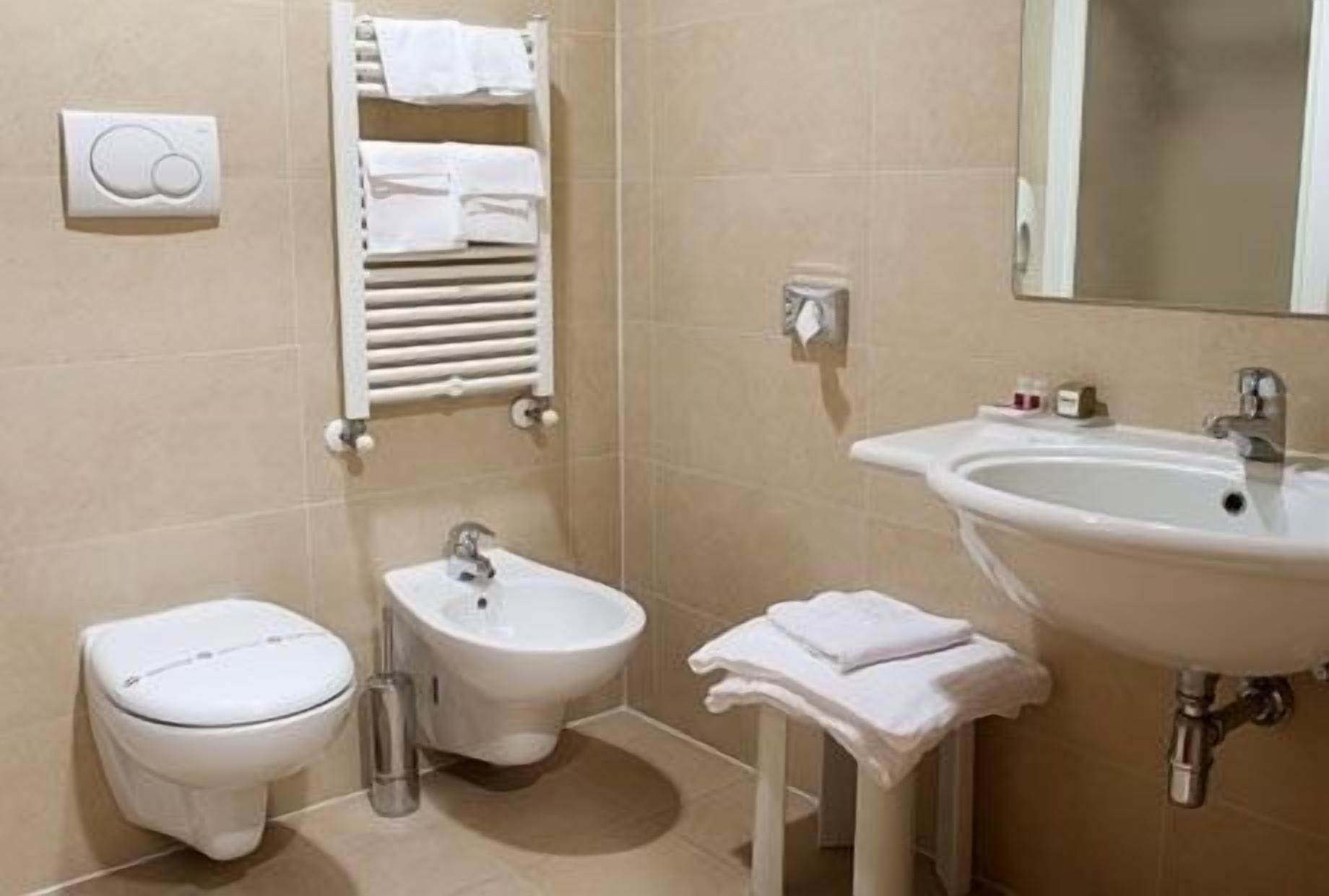 Een badkamer met toilet, bidet, wastafel en handdoekhouder.