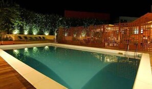 A swimming pool with a wooden deck and a fence with a lattice design.