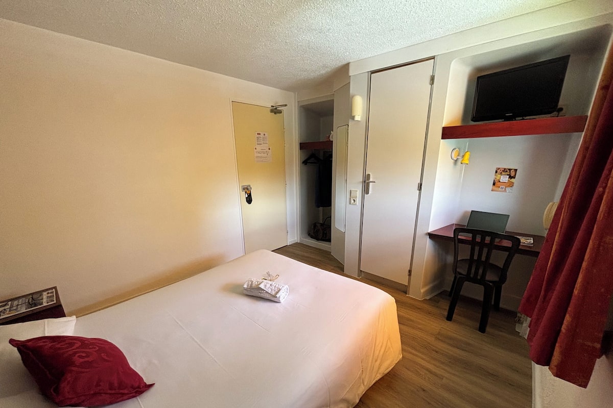 A hotel room with a bed, a desk, a chair, a TV, and a wardrobe.