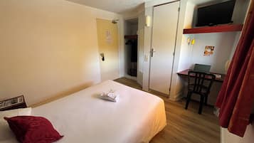 A hotel room with a bed, a desk, a chair, a TV, and a wardrobe.
