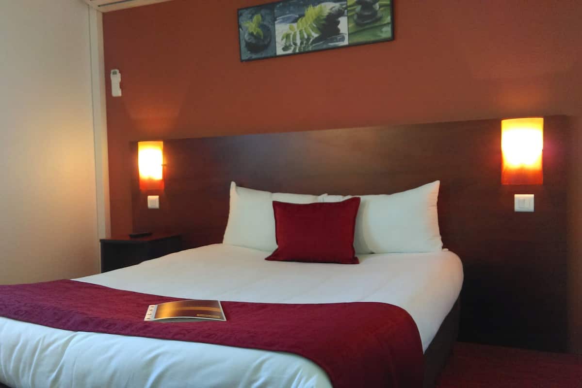 A hotel room with a large bed, two bedside lamps, a nightstand, and a painting on the wall.