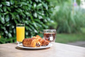 Un croissant en un plato con un vaso de jugo de naranja y un vaso de té sobre una mesa de madera.