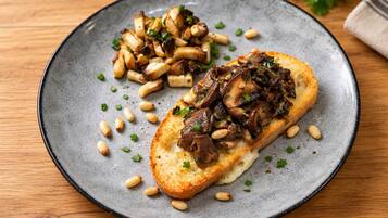 Un plat amb una torrada coberta de bolets i pinyons, i una guarnició de patates rostides.