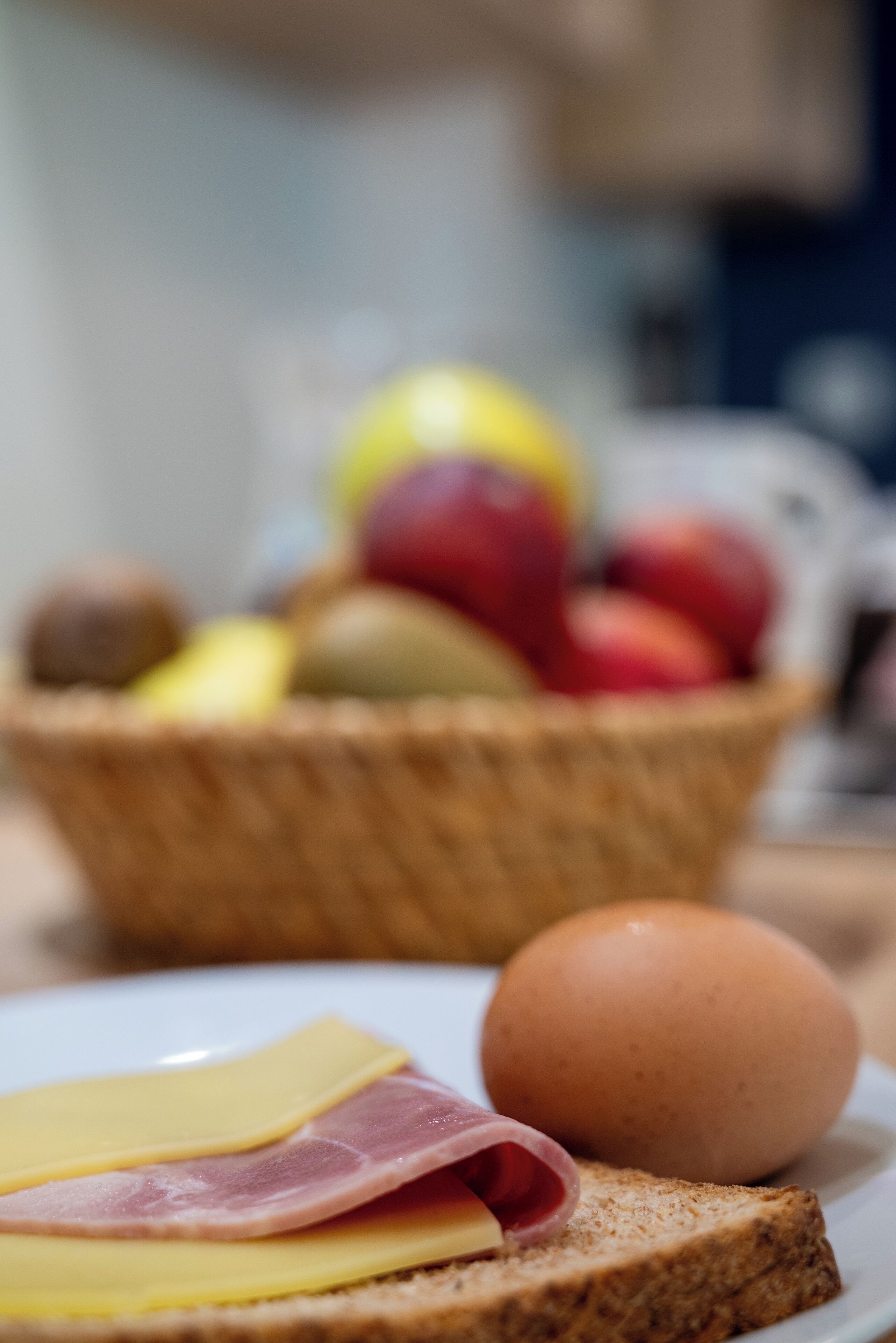 A basket of fruits and a plate with toast, cheese, and ham.