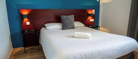 A neatly made bed with white linens and a grey pillow, two bedside tables with lamps, and a wooden headboard.