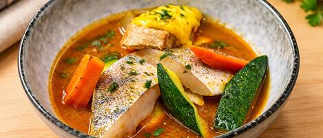 A bowl of fish stew with vegetables.