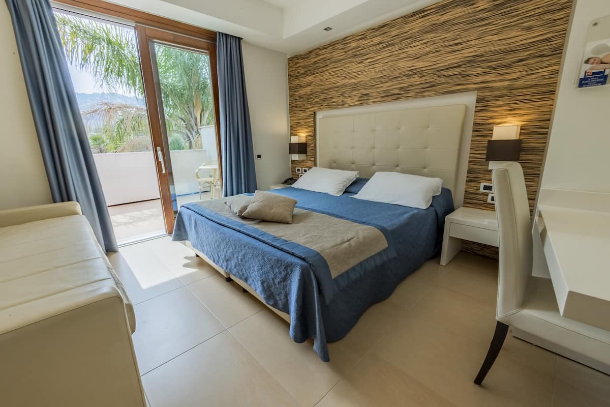 A modern hotel room with a large bed, a desk, and a view of the outdoors.