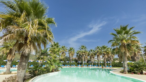 A pool area with palm trees, blue lounge chairs, and umbrellas. - Prince Franklyn Hotel (Castellabate)