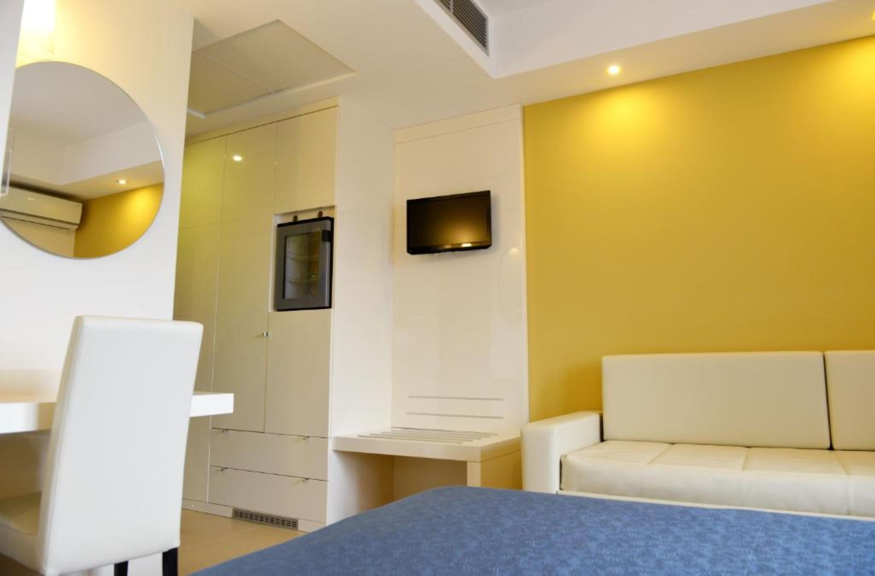 Ein modernes Schlafzimmer mit einem Bett, einem weißen Sessel, einer Couch, einem Fernseher und einem Spiegel.