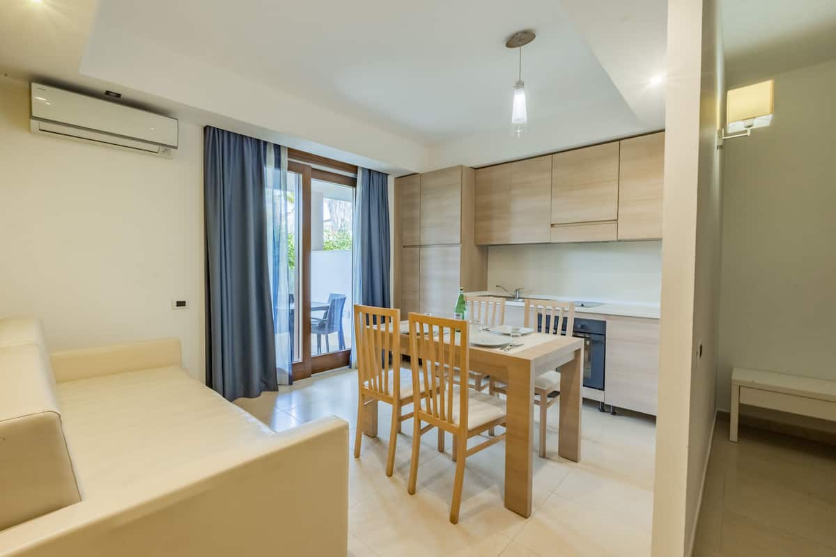 A modern living room with a sofa, dining table, and chairs. There is a kitchen area with cabinets and a sink.