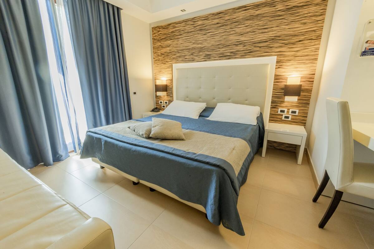 A modern hotel room with a large bed, a desk, and a chair.