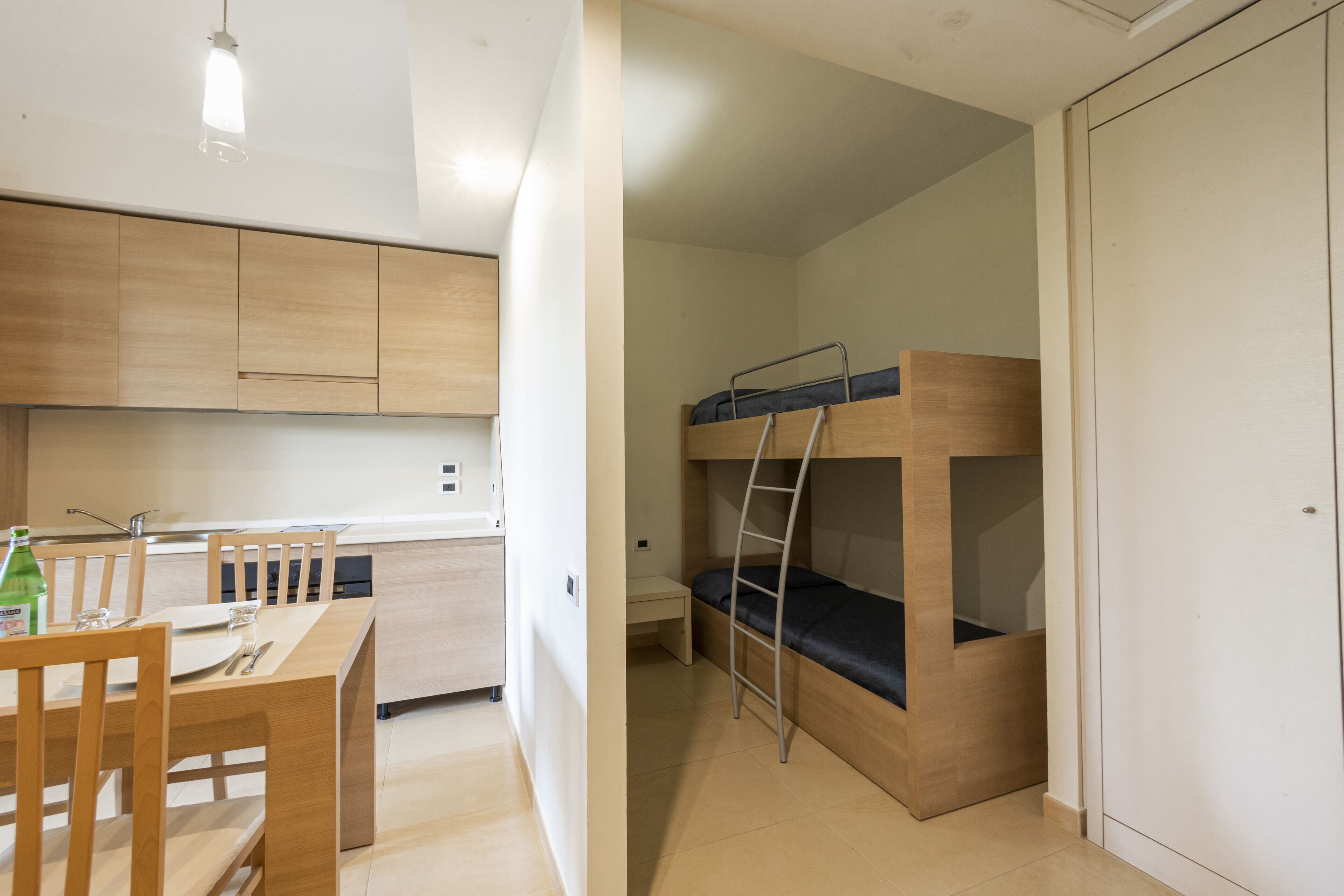 Una stanza compatta con un letto a castello, una piccola cucina con mobili in legno e un tavolo da pranzo con sedie.