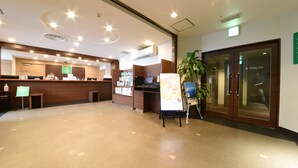 Zona de recepción de un hotel con un mostrador de madera, una pantalla digital y una planta.