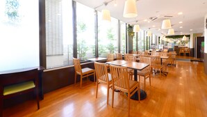Un restaurante espacioso con mesas y sillas de madera, ventanas amplias e iluminación colgante.