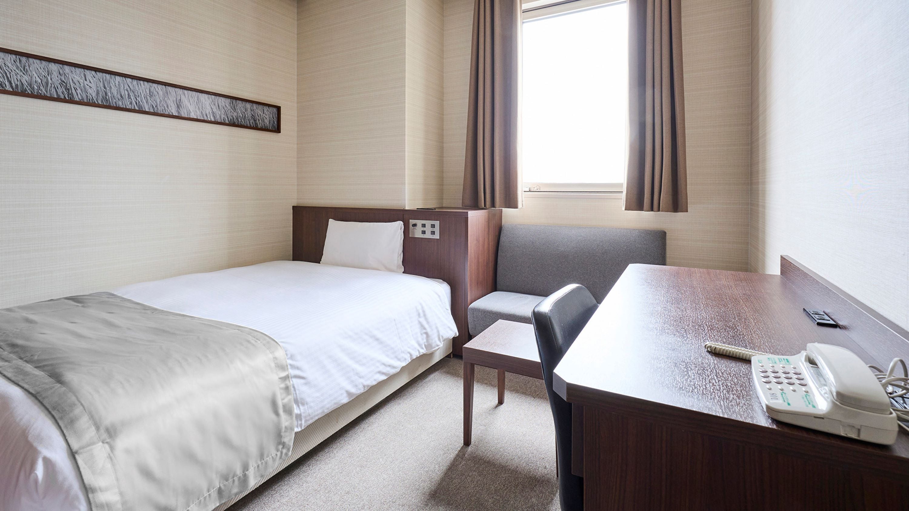 A hotel room with a bed, a desk with a telephone, and a chair.