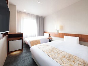 Habitación de hotel con dos camas, televisión, refrigerador pequeño, mesita de noche y ventana con cortinas.