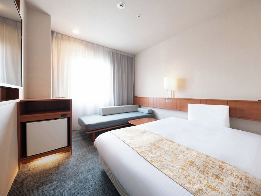 A hotel room with a bed, a desk, a seating area, and a television.