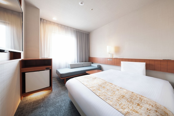 Habitación de hotel con cama, escritorio, zona de estar y televisión.