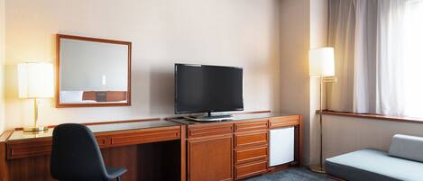 A hotel room with a wooden desk, a television, a chair, a bed, and a window with curtains.