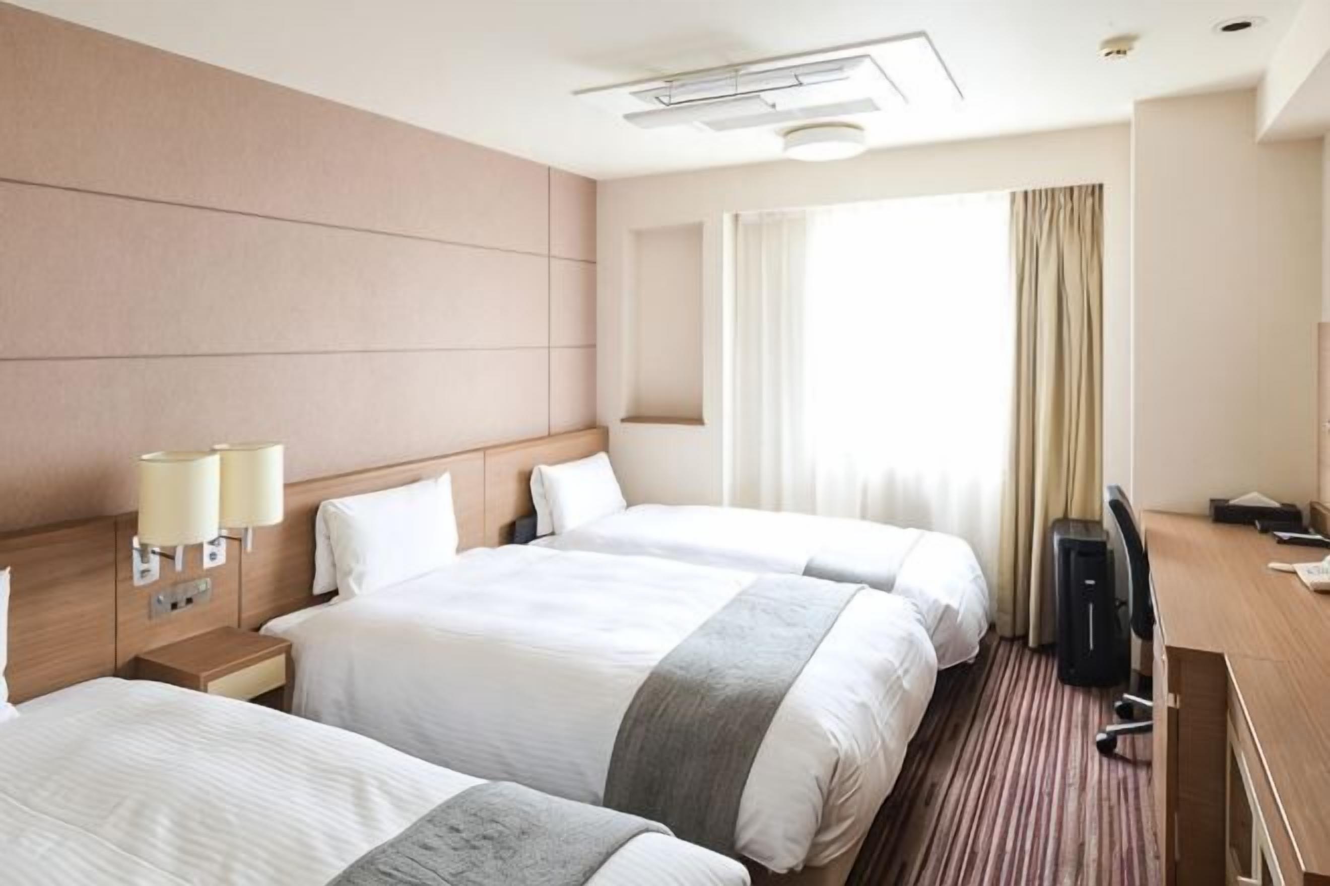 A hotel room with two beds, a desk, a chair, a TV, and a window with curtains.