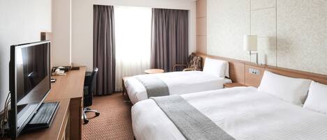 A hotel room with two beds, a desk with a TV, a chair, a lamp, and a window with curtains.