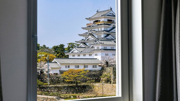 A traditional Japanese castle with multiple tiers and a white facade, viewed through a window. - Vessel Inn Fukuyama Station (Fukuyama)