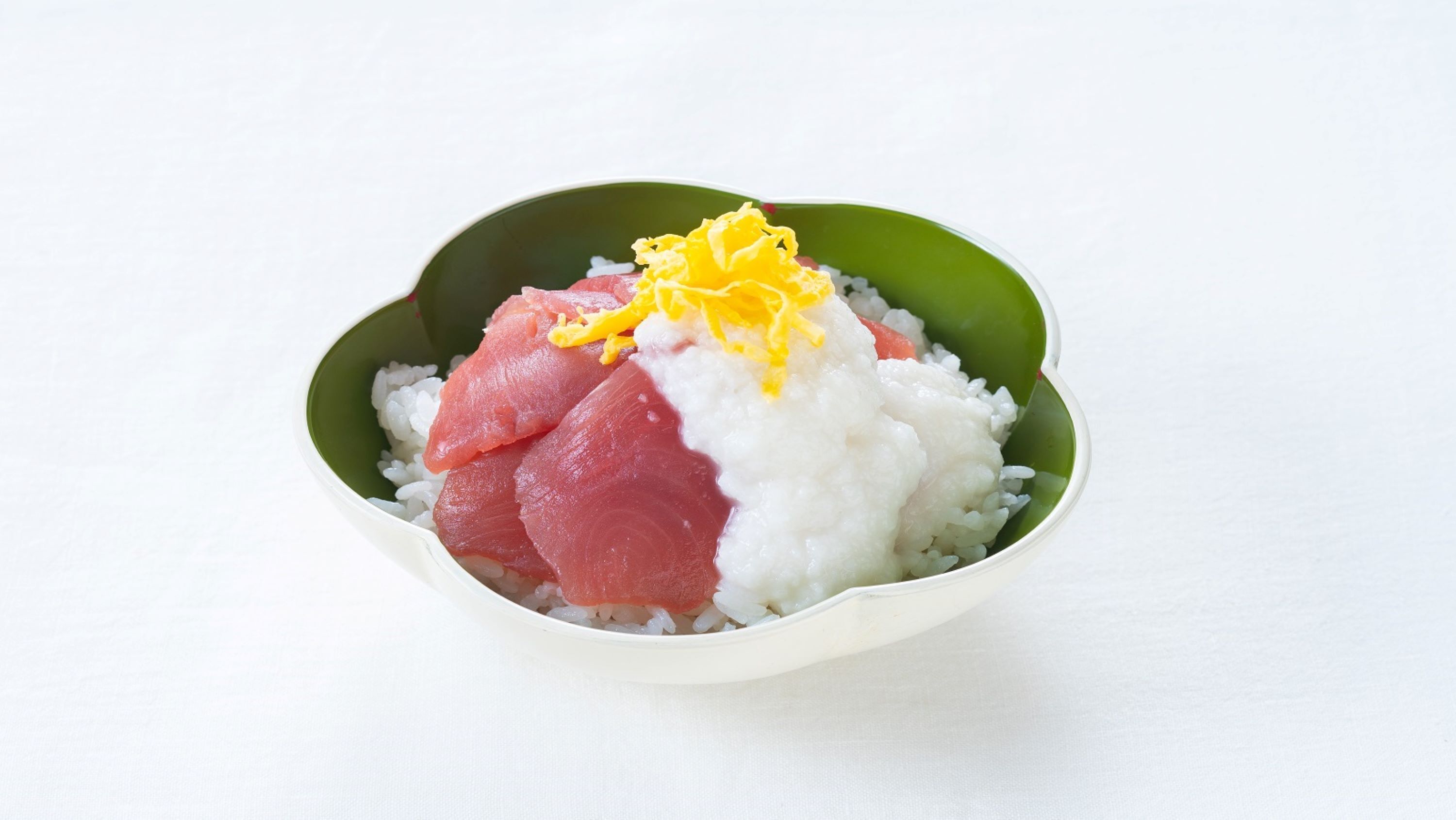 Un bol de sushis composé de riz, de poisson et d’une garniture jaune râpée.