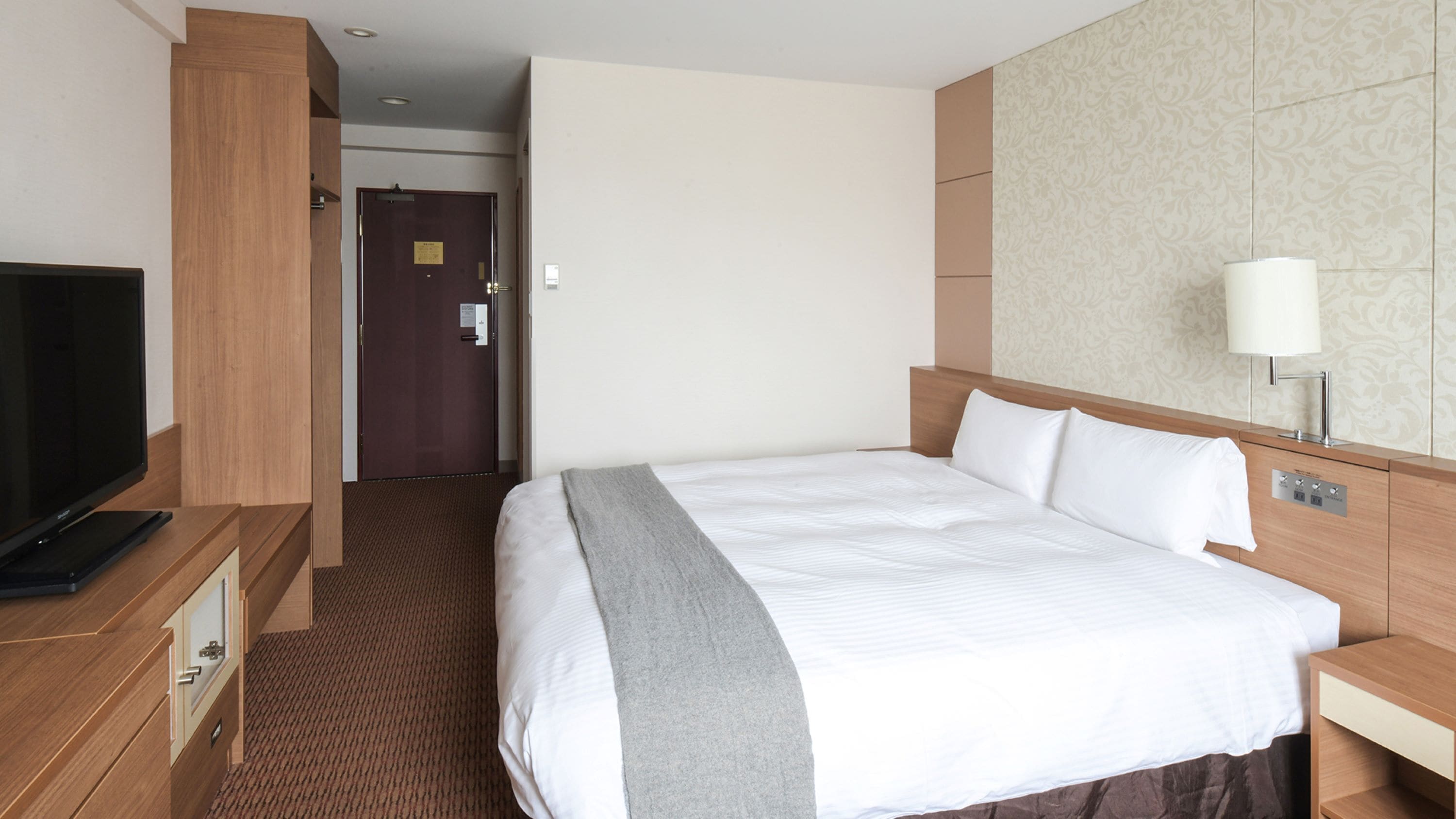 Una habitación de hotel con una cama, televisor, escritorio y lámpara.