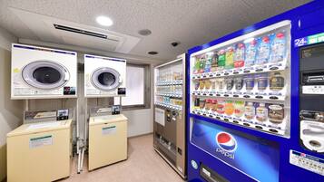 Una lavanderia con due asciugatrici, una macchina distributrice di bevande e un frigorifero Pepsi.
