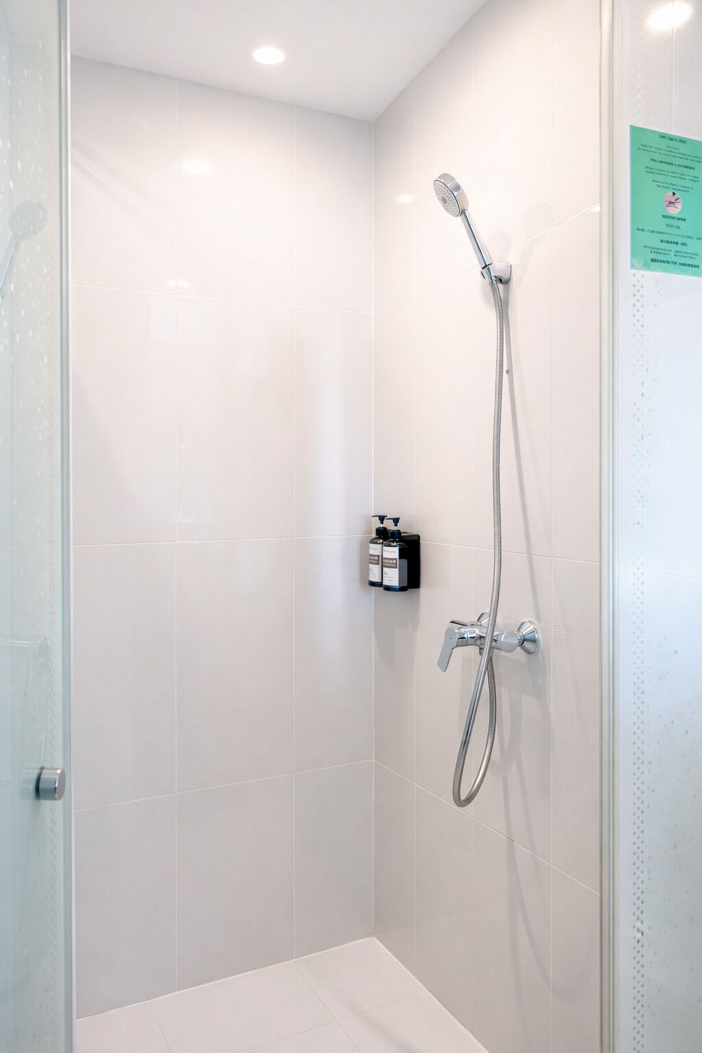 Een kleine, moderne badkamer met witte tegels en een glazen deur.