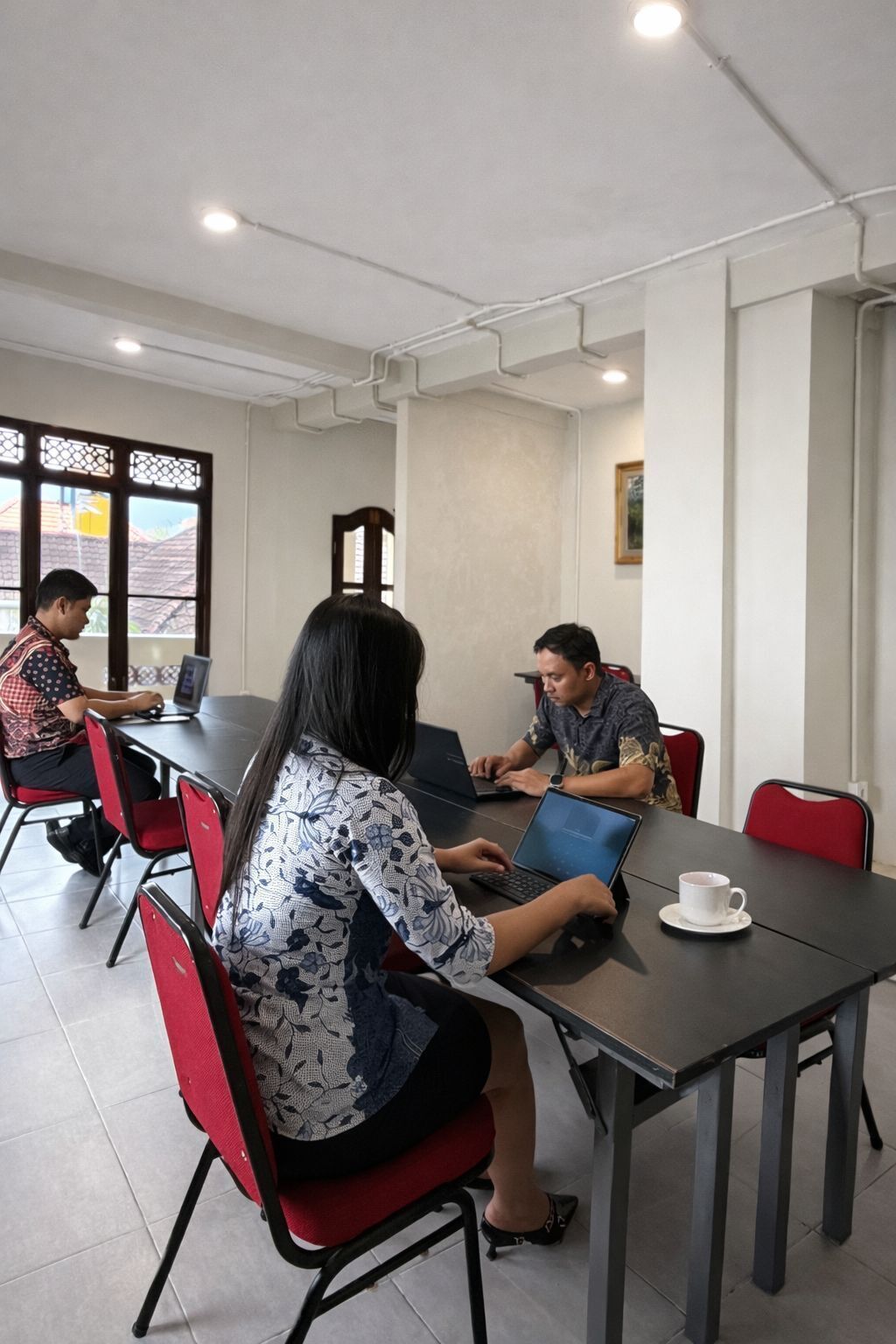 A conference room with four people working at a table, equipped with laptops and a white cup.