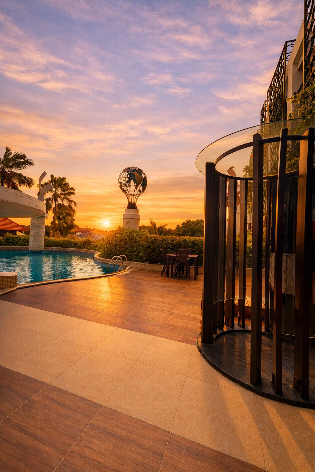 A pool area with a sunset view, a globe sculpture, and a covered seating area.
