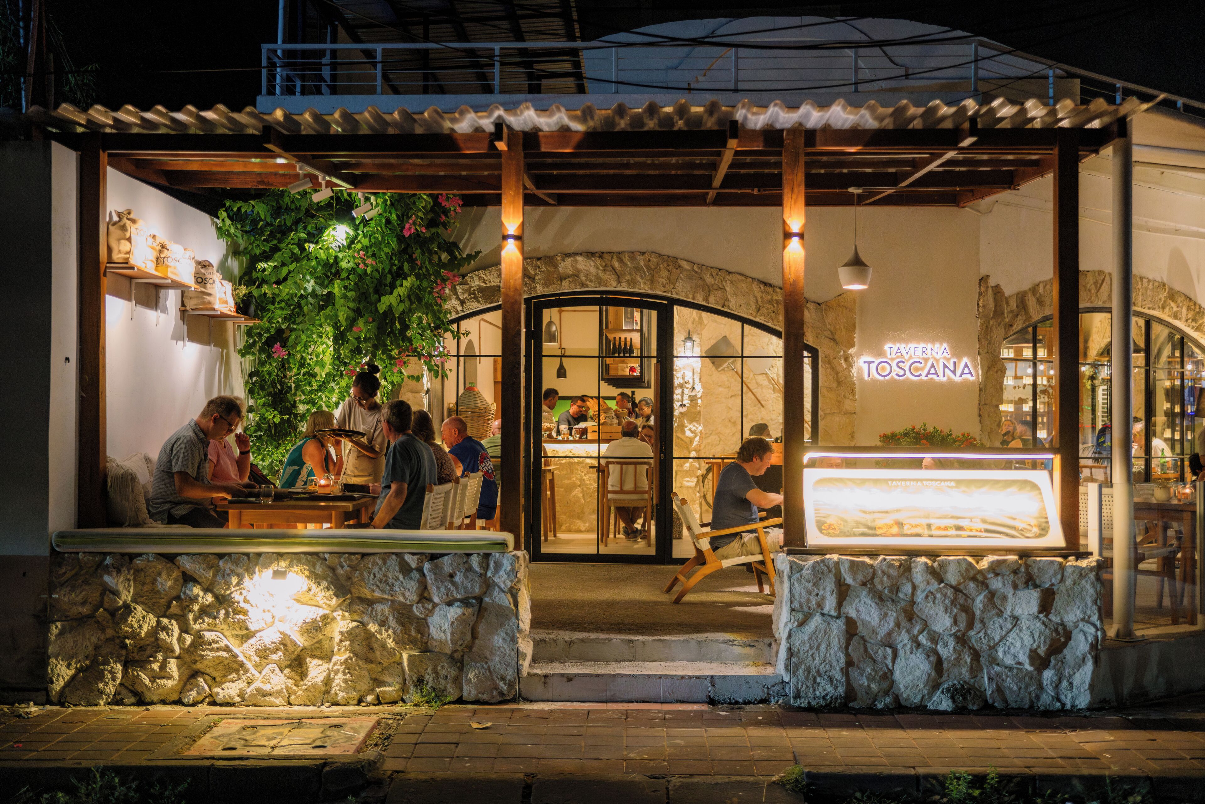 Un restaurant à la façade en pierre, doté d’une terrasse et d’une enseigne indiquant « TAVERNA TOSCANA ».