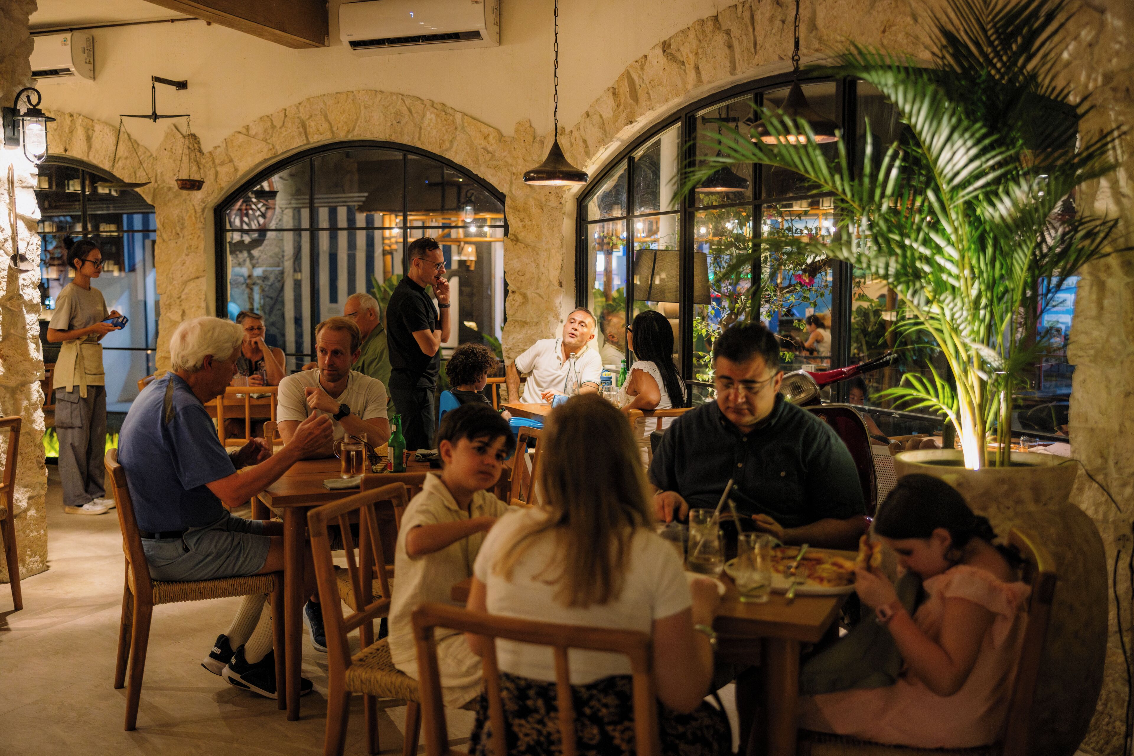 A restaurant with stone arches, wooden tables, and a mix of seated and standing guests.