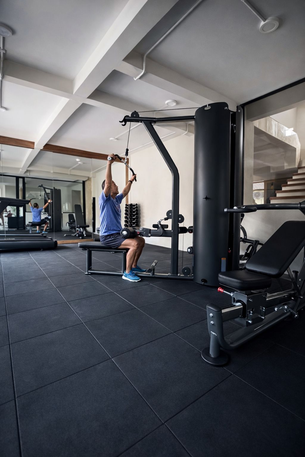 A gym with a person using a pull-up bar, a weight bench, and various exercise equipment.