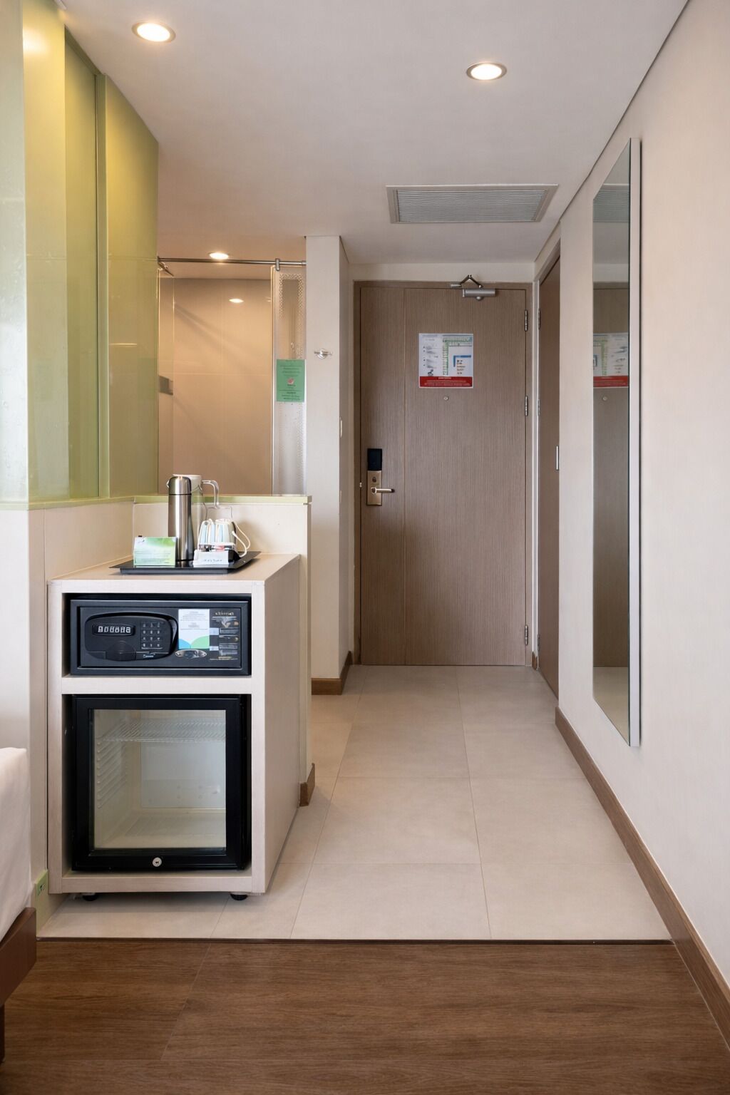 A hotel corridor with a reception area, a wooden door, and a mirror on the wall.