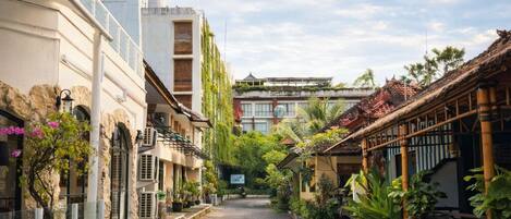 A paved pathway flanked by buildings with a mix of modern and traditional architecture, leading towards a distant structure.