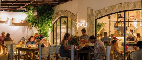 An outdoor dining area with tables and chairs, a stone wall, and a sign reading "Taverna Toscana".
