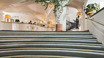 Eine imposante Treppe mit geschwungener Form, die zu einem Empfangsbereich mit Theke und Zimmerpflanzen führt.