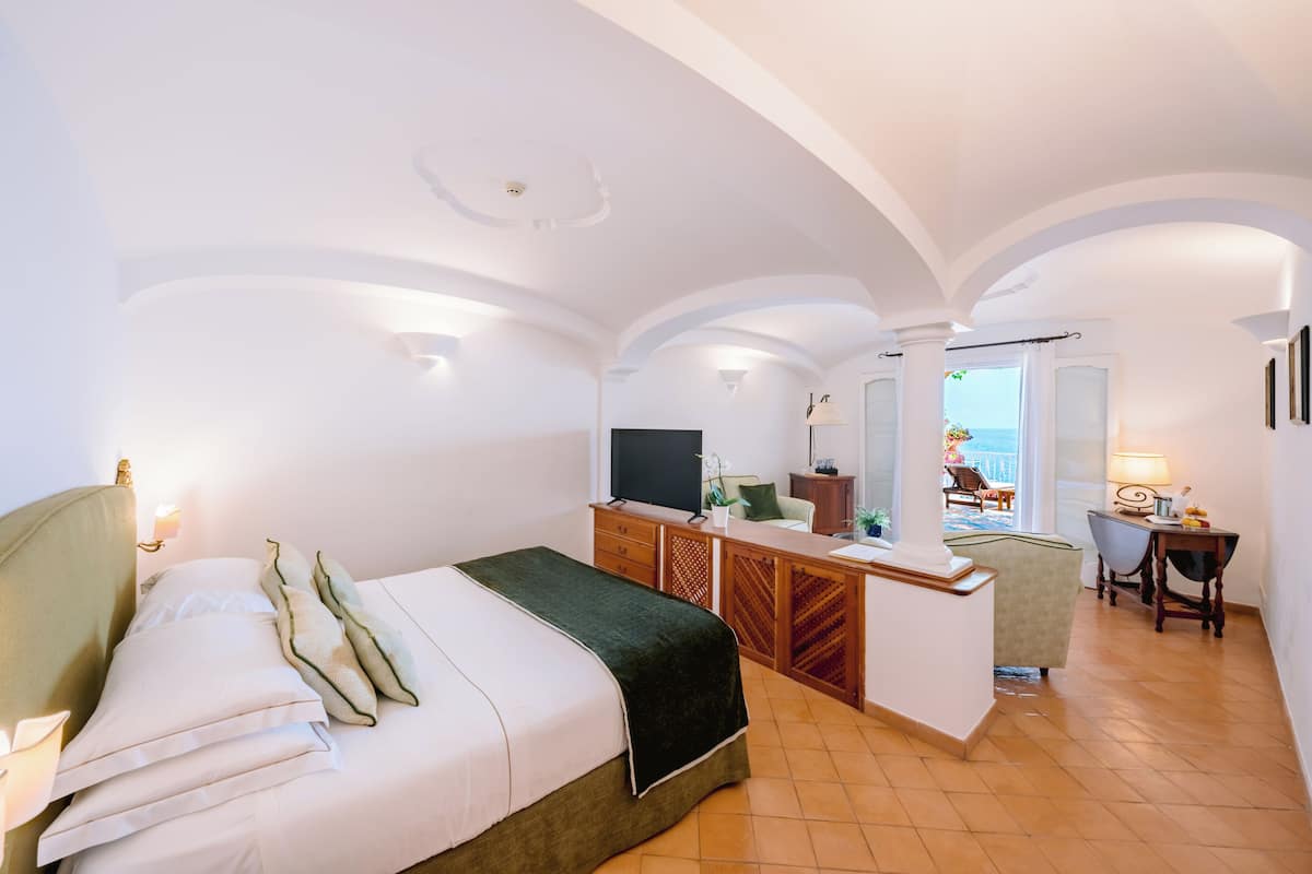 A hotel room with a bed, desk, chair, and a view of the sea.