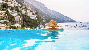 Une piscine où une personne porte un chapeau de paille, entourée de bâtiments sur une colline.
