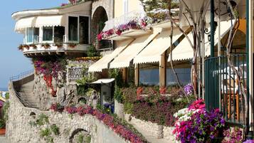 A stone building with balconies adorned with flowers, a sign reading "Covo dei Saraceni," and a staircase leading up to the entrance.