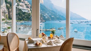 Une table à manger dressée avec des aliments pour le petit-déjeuner, donnant sur une ville côtière et la mer.