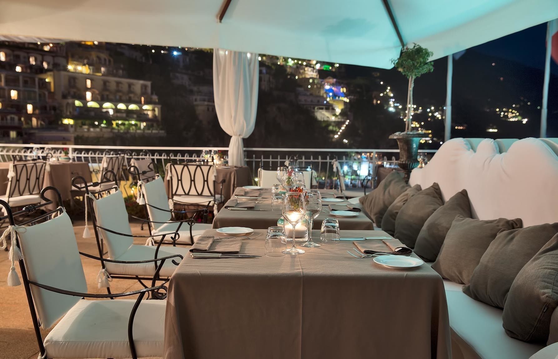 An outdoor dining area with tables set for two, chairs, and a sofa.