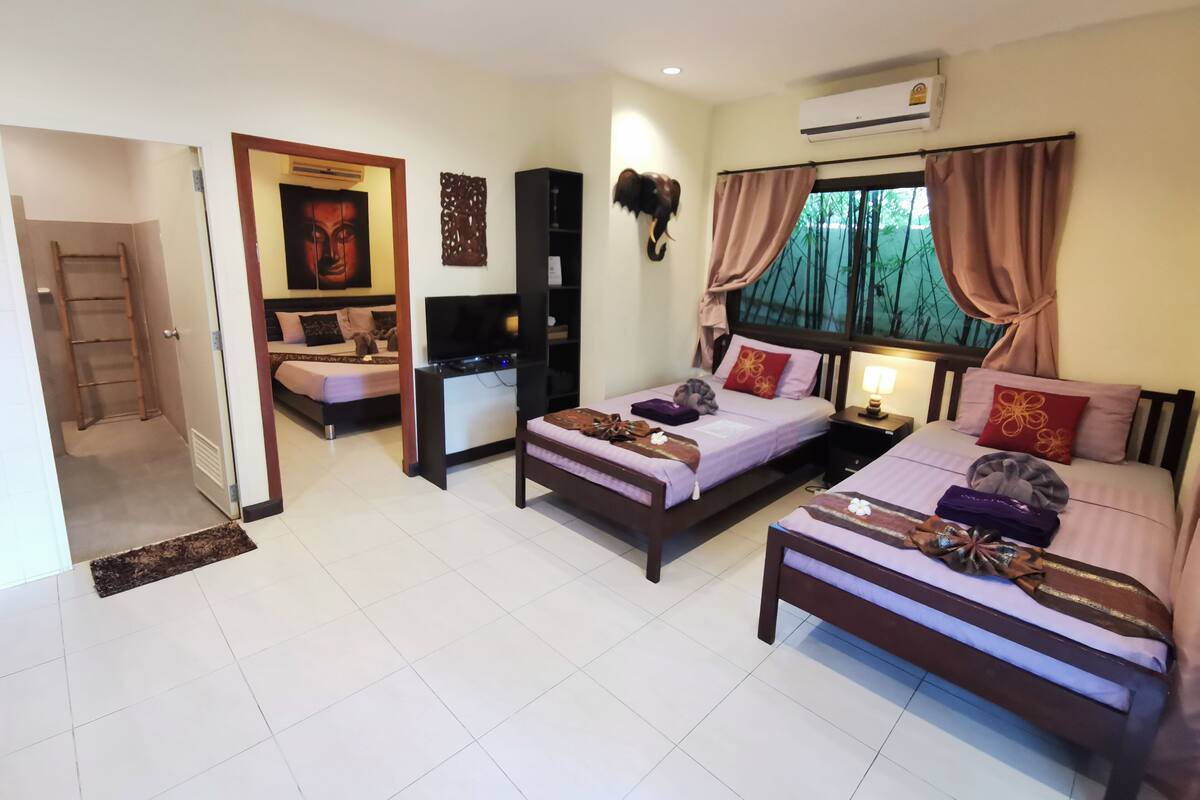 A hotel room with two single beds, a desk, a TV, and an air conditioning unit.