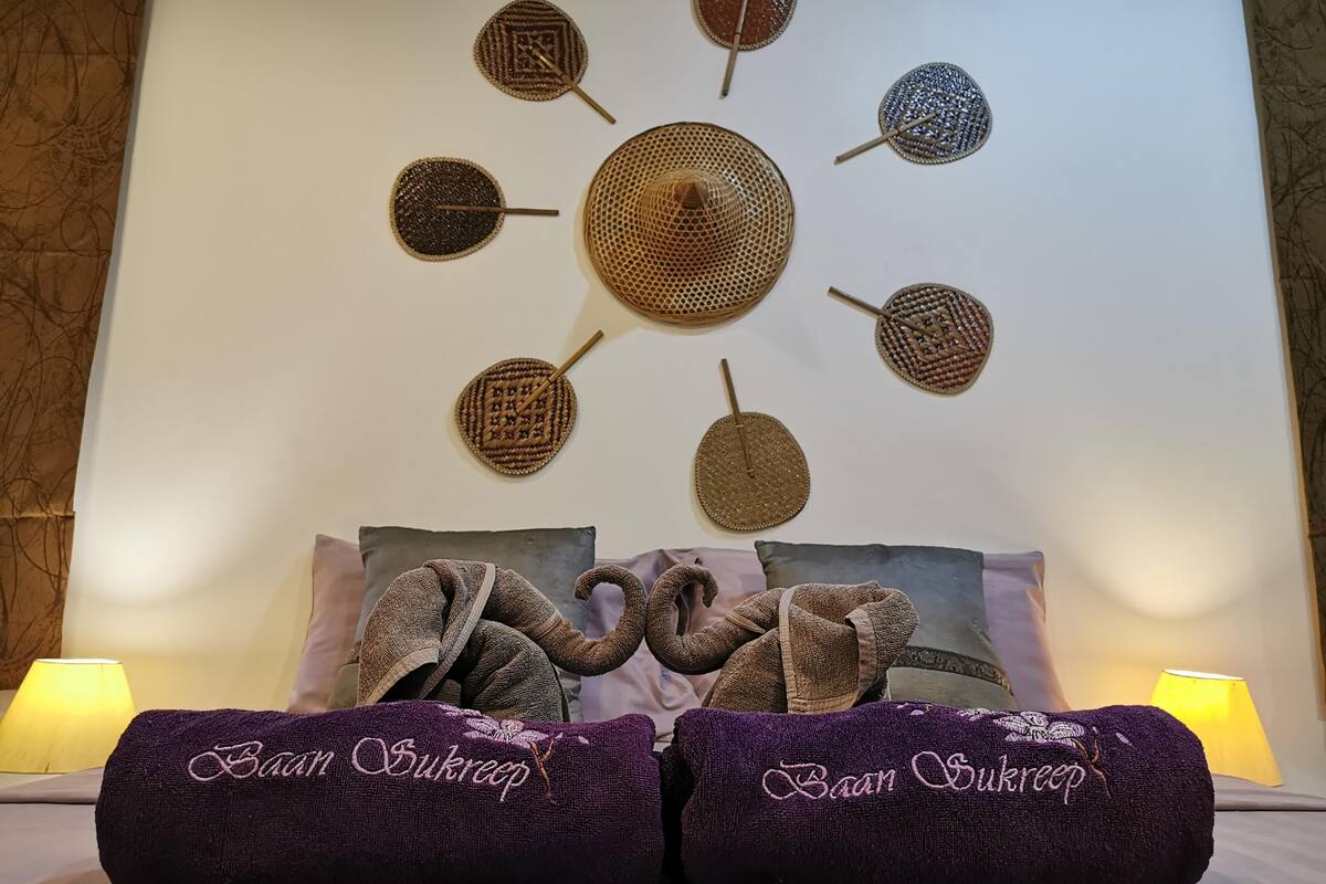 A bed with two purple towels, a wall with woven art pieces, and two lamps on either side.