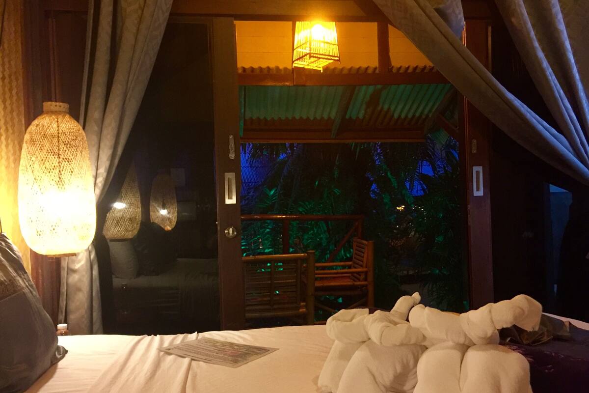 A bedroom with a bed, pillows, a lamp, and a view of the outside.