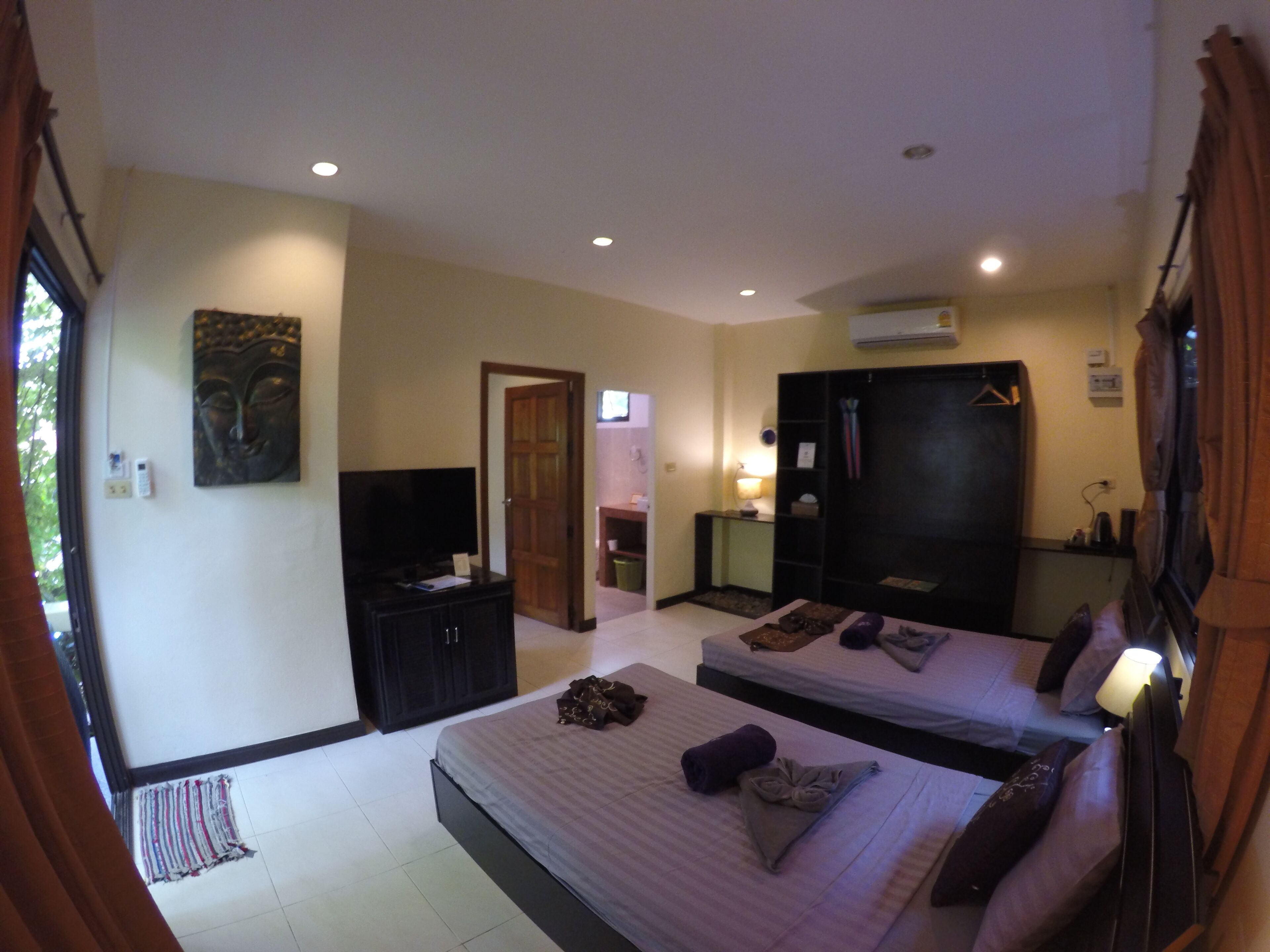 Habitación de hotel con dos camas, un televisor, un armario y un baño visible a través de una puerta abierta.