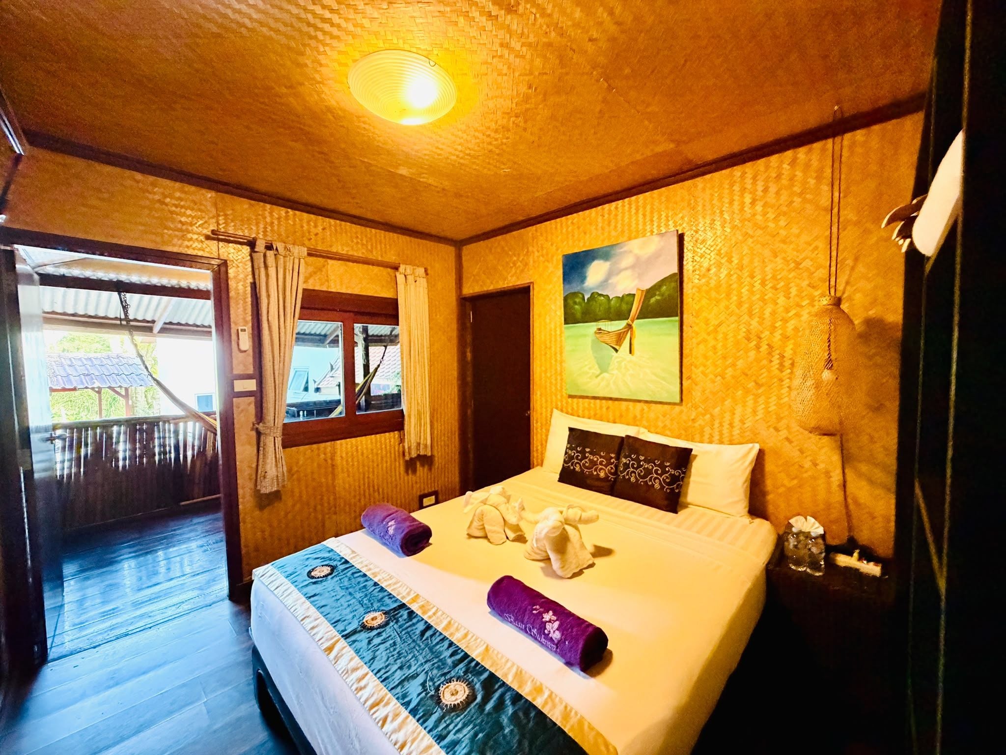 A hotel room with a bed, a painting, and a view of the outside.